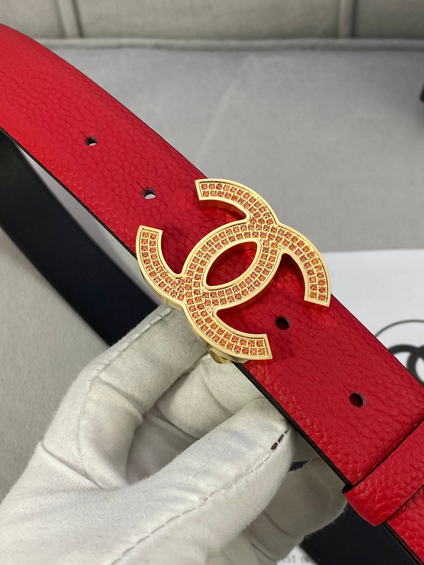 Red leather belt close-up with gold CC-style buckle and small eyelet holes