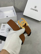 Brown leather belt with gold CC buckle, held in a white-gloved hand