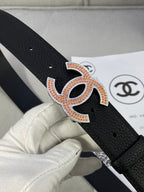 Close-up of black leather belt with orange-and-gold rhinestone CC logo buckle.