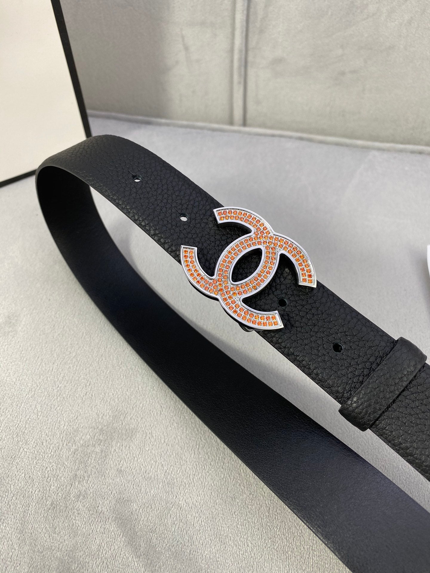 Black leather belt with orange-gold rhinestone CC buckle, strap stretched flat.