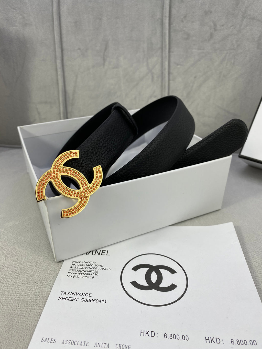 Black leather belt with large gold CC logo buckle on textured strap, shown in box.