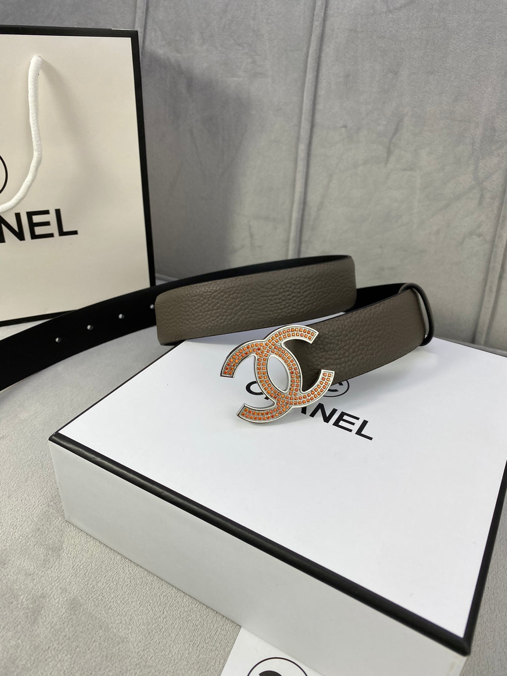 Chanel belt with dark taupe strap and gold CC buckle, styled on a gift box