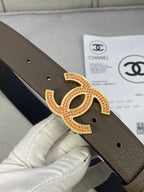 Chanel belt close-up on gold CC buckle set with red and clear stones on dark taupe