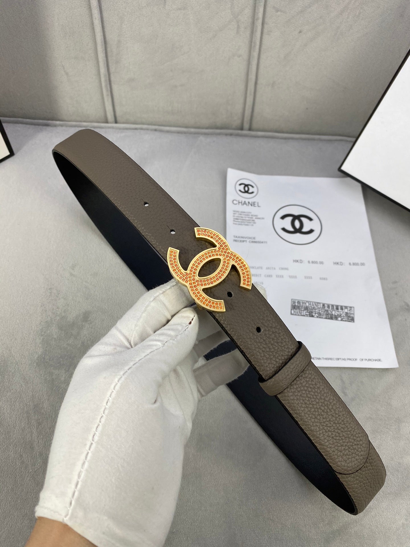 Chanel belt held in a hand: dark taupe leather strap with gold CC buckle