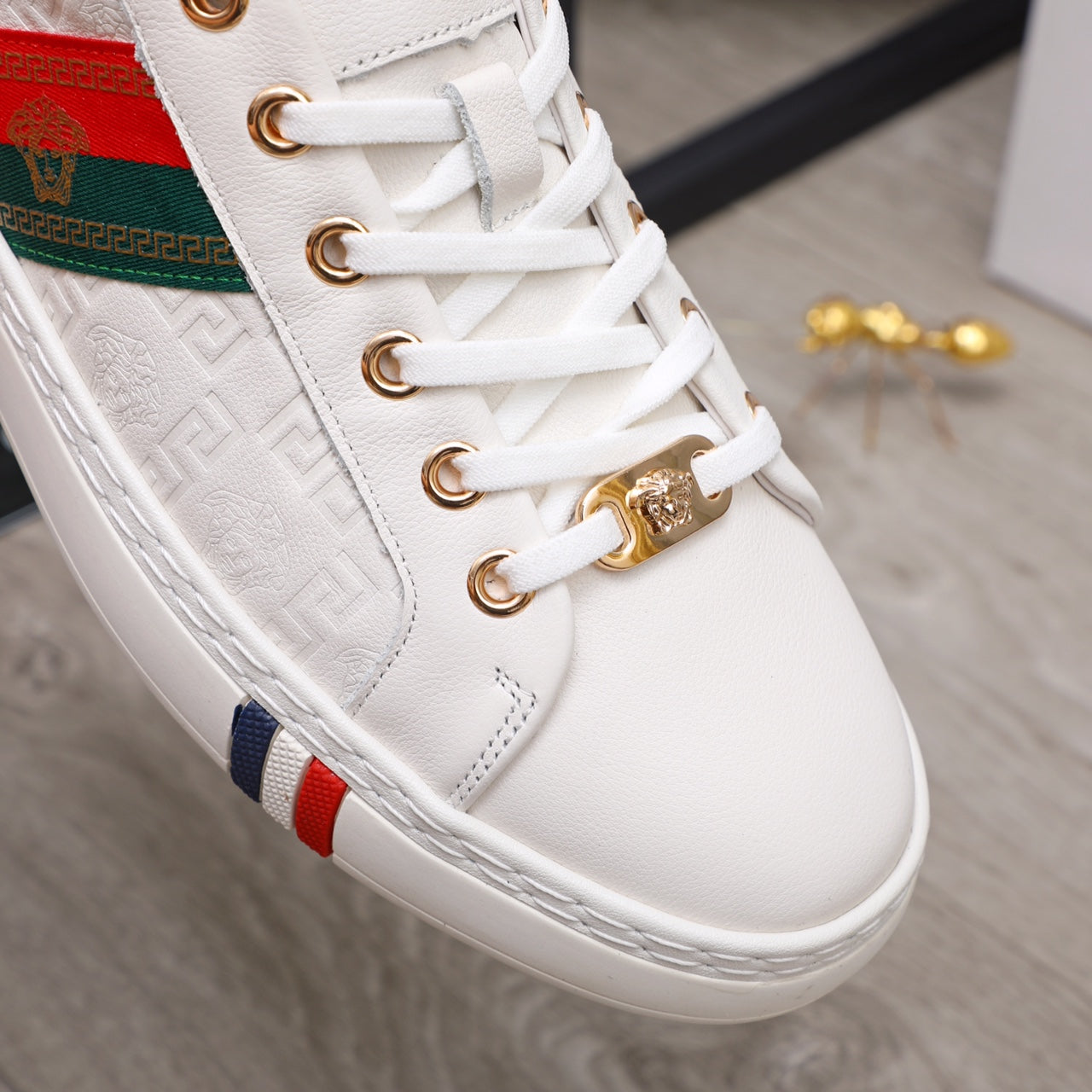 Close-up of white sneakers: gold lace eyelets, multicolor stripe panel, textured side