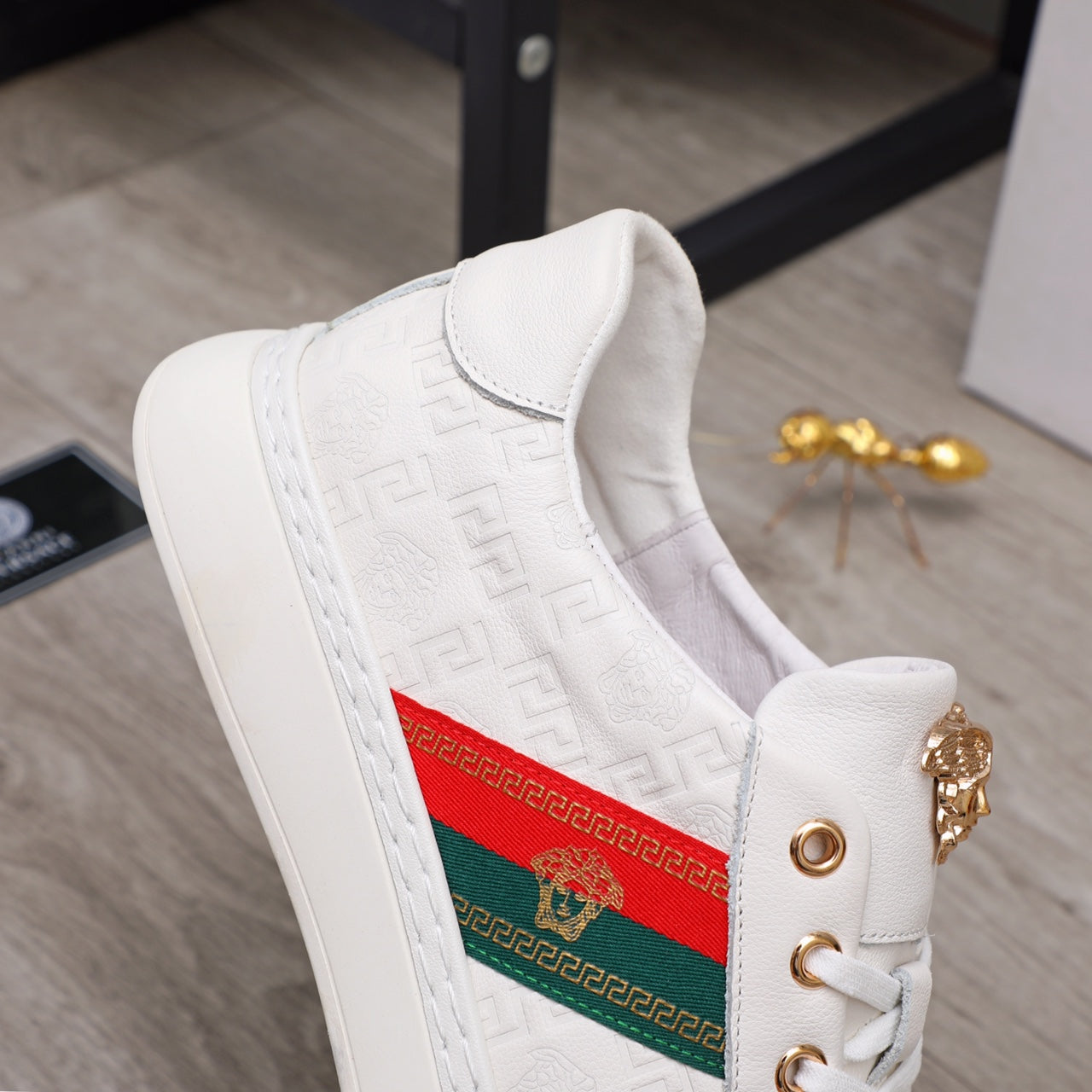 White sneaker side view with embossed pattern, multicolor stripe panel and gold hardware