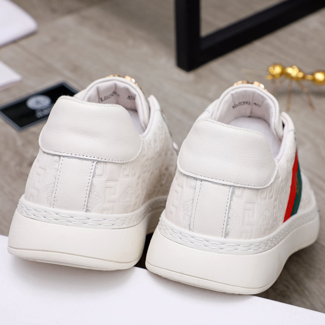 White sneakers rear view with padded collar and gold emblem detail on the heel