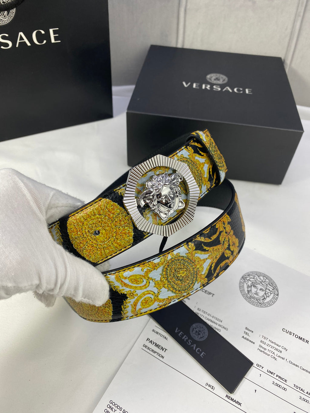 Versace baroque-print belt with gold Medusa buckle, held by white-gloved hand