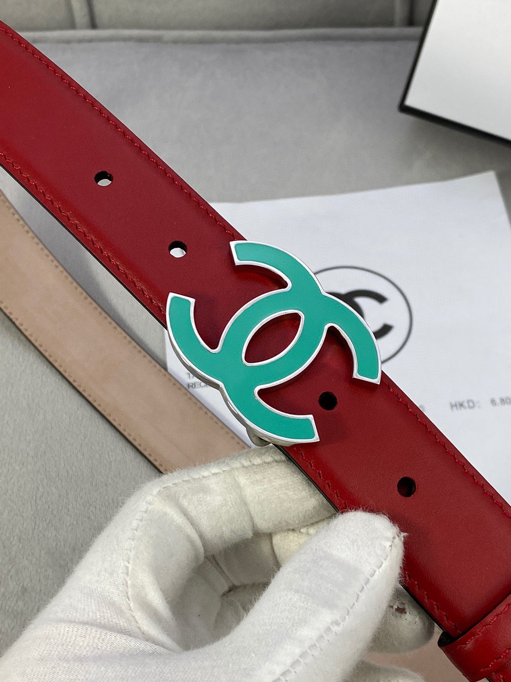 Red leather belt close-up: teal CC-logo buckle and two pin holes
