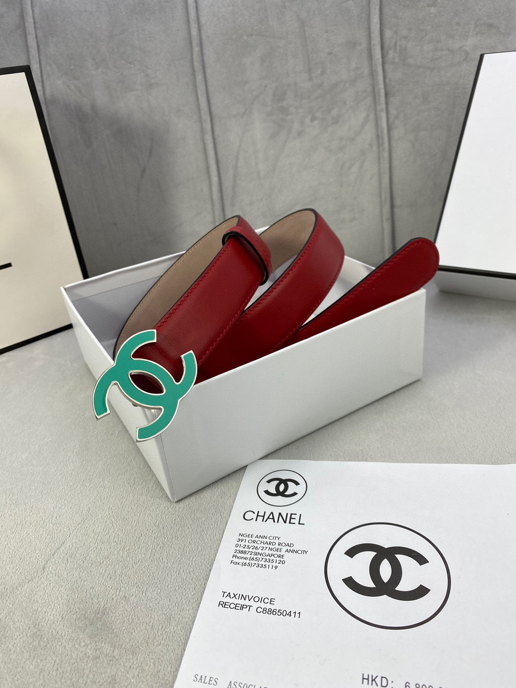 Red leather belt with teal CC-logo buckle, coiled in box with tag