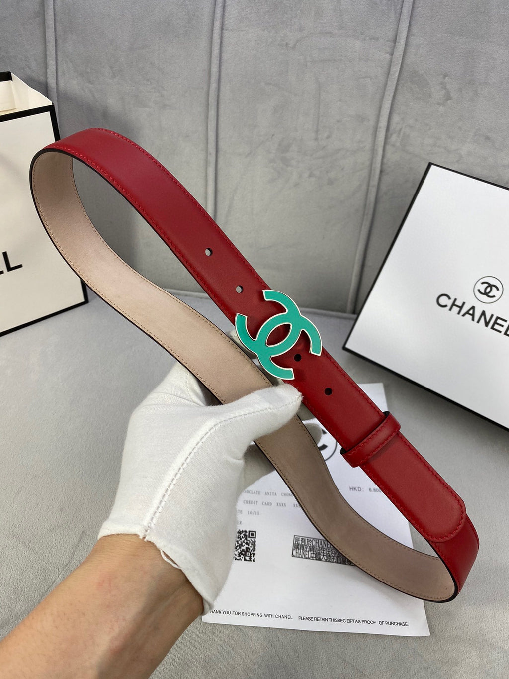 Red leather belt with teal CC-logo buckle, side view with tan underside