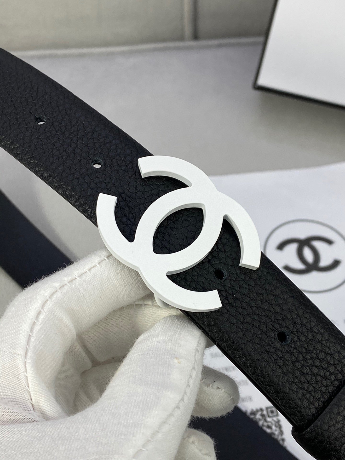 Chanel belt close-up, black textured strap with silver CC buckle and punched holes.