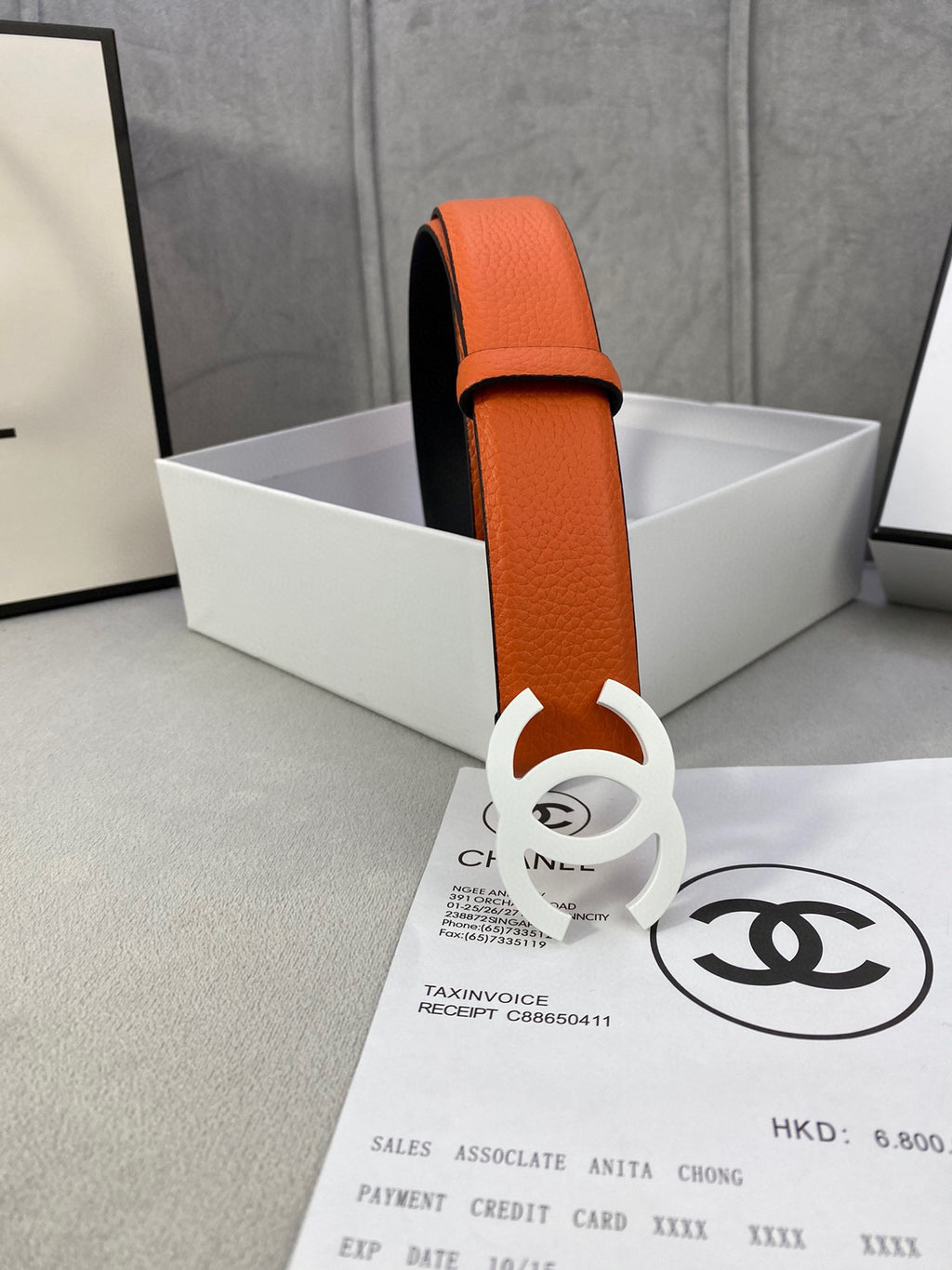 Chanel leather belt standing upright with orange strap and white CC buckle