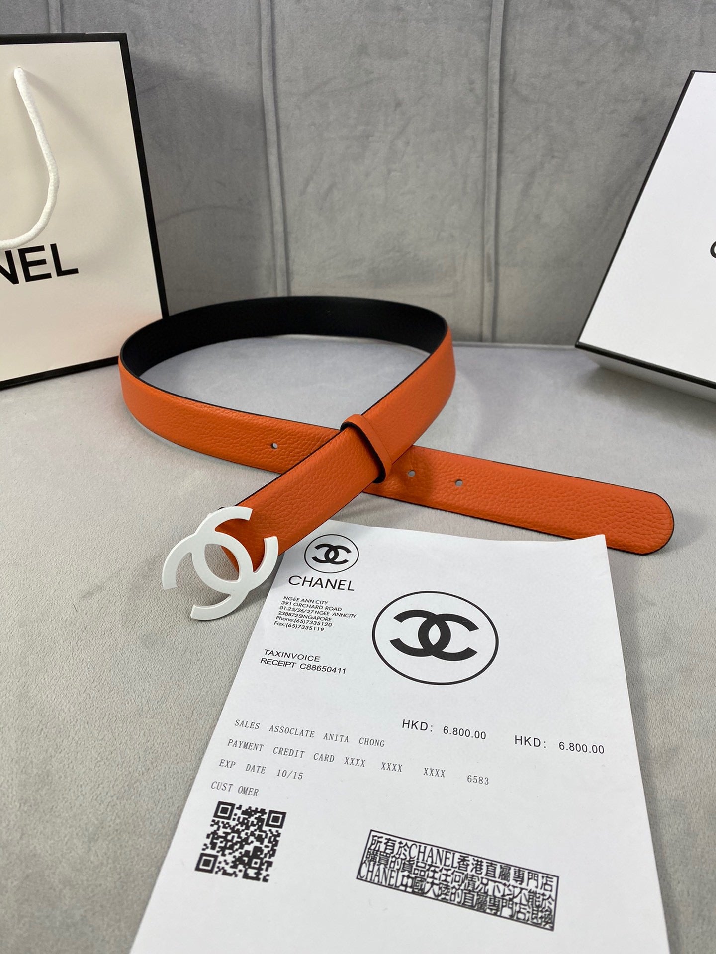 Chanel belt laid flat with orange leather strap and white CC buckle, shown with invoice
