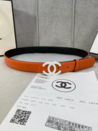 Chanel belt with orange leather strap and white CC buckle, resting on black lining