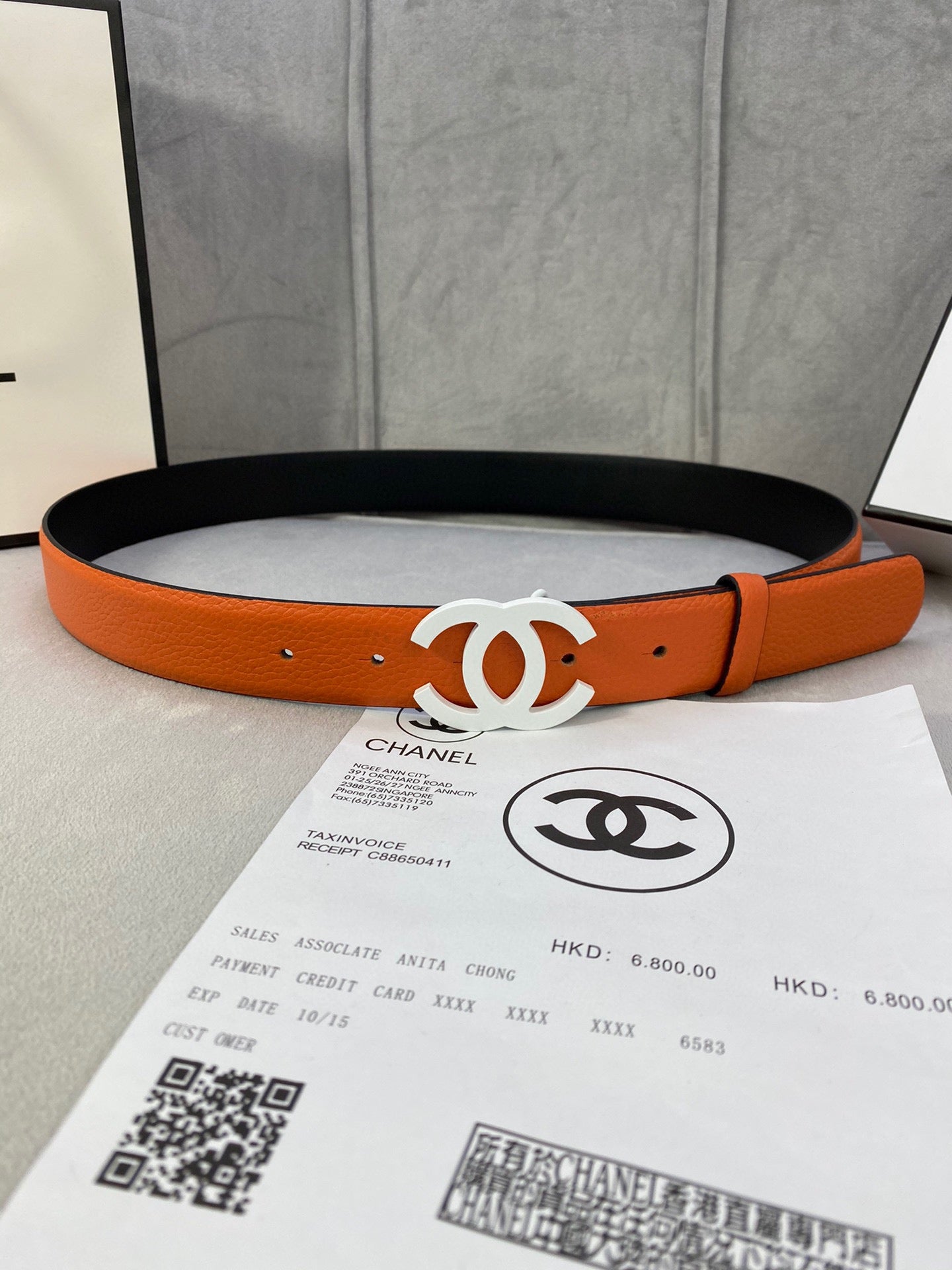 Chanel belt with orange leather strap and white CC buckle, resting on black lining