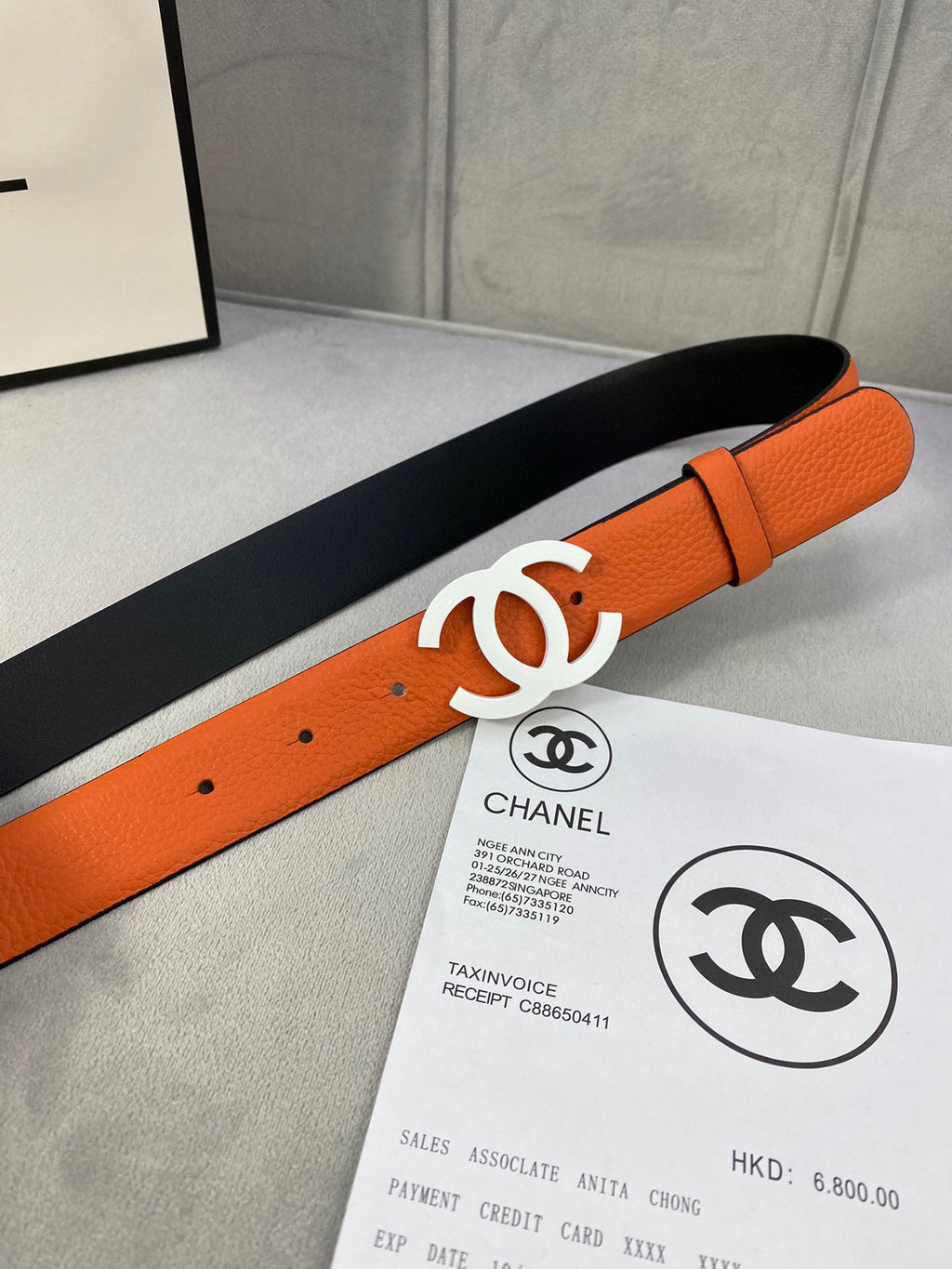 Chanel leather belt angled view with orange strap and white CC buckle