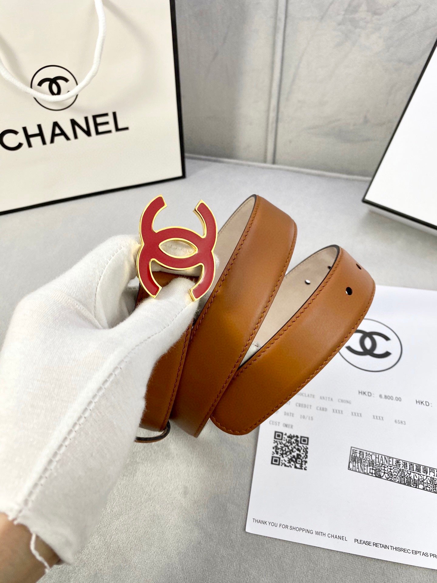 Brown Chanel belt with red CC buckle shown near retail packaging