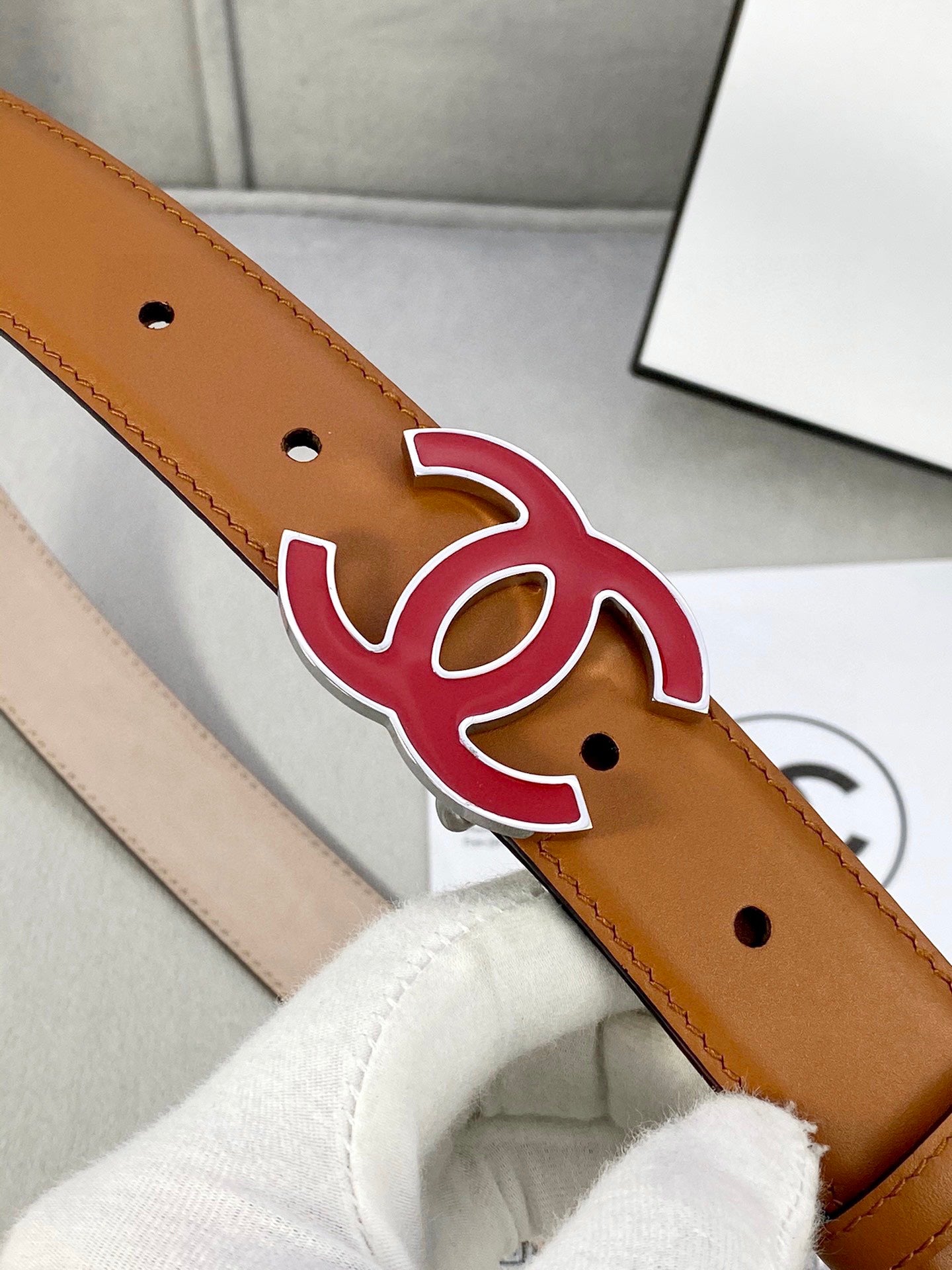 Close-up of brown Chanel belt with red CC emblem and strap hole perforations