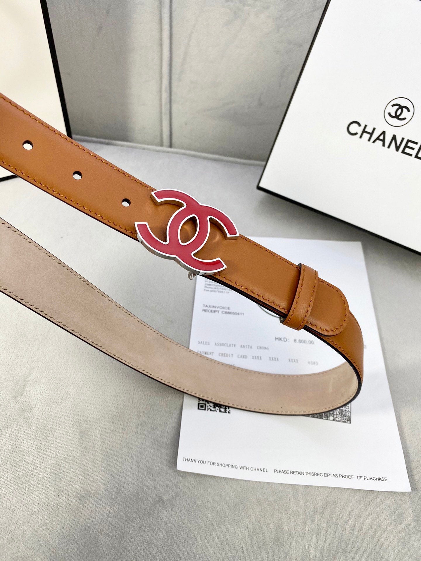 Close-up of brown Chanel belt strap with red CC buckle and hole lining