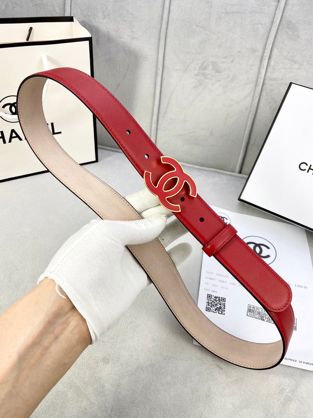 Red leather belt with Chanel CC logo buckle, shown from side while held by hand