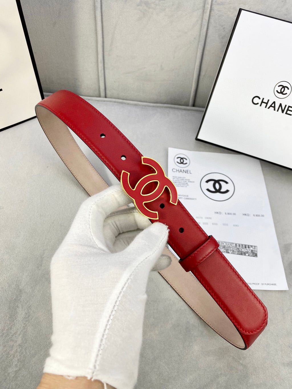Red leather belt held in hand, with Chanel CC logo buckle and gold-tone hardware