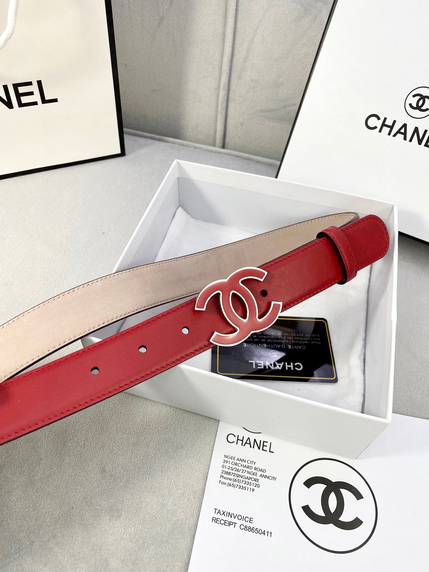 Red leather belt with Chanel CC logo buckle, laid across packaging box