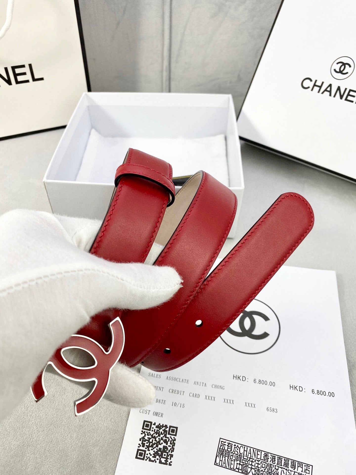 Red leather belt with Chanel CC logo buckle and gold-tone hardware, coiled in box