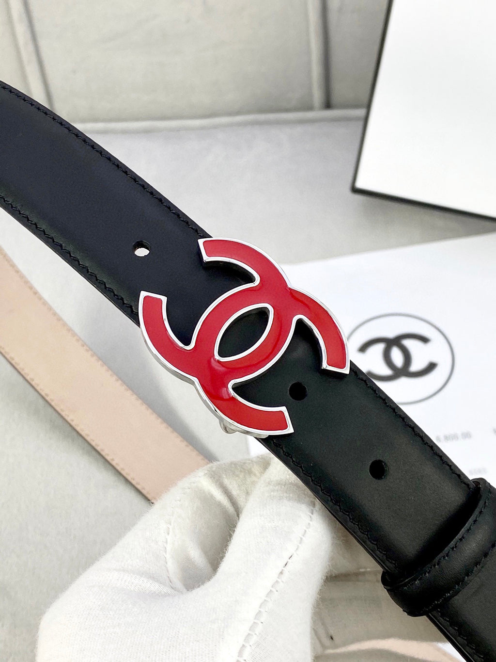 Chanel belt close-up: dark leather strap with red-and-black CC emblem and punched holes.