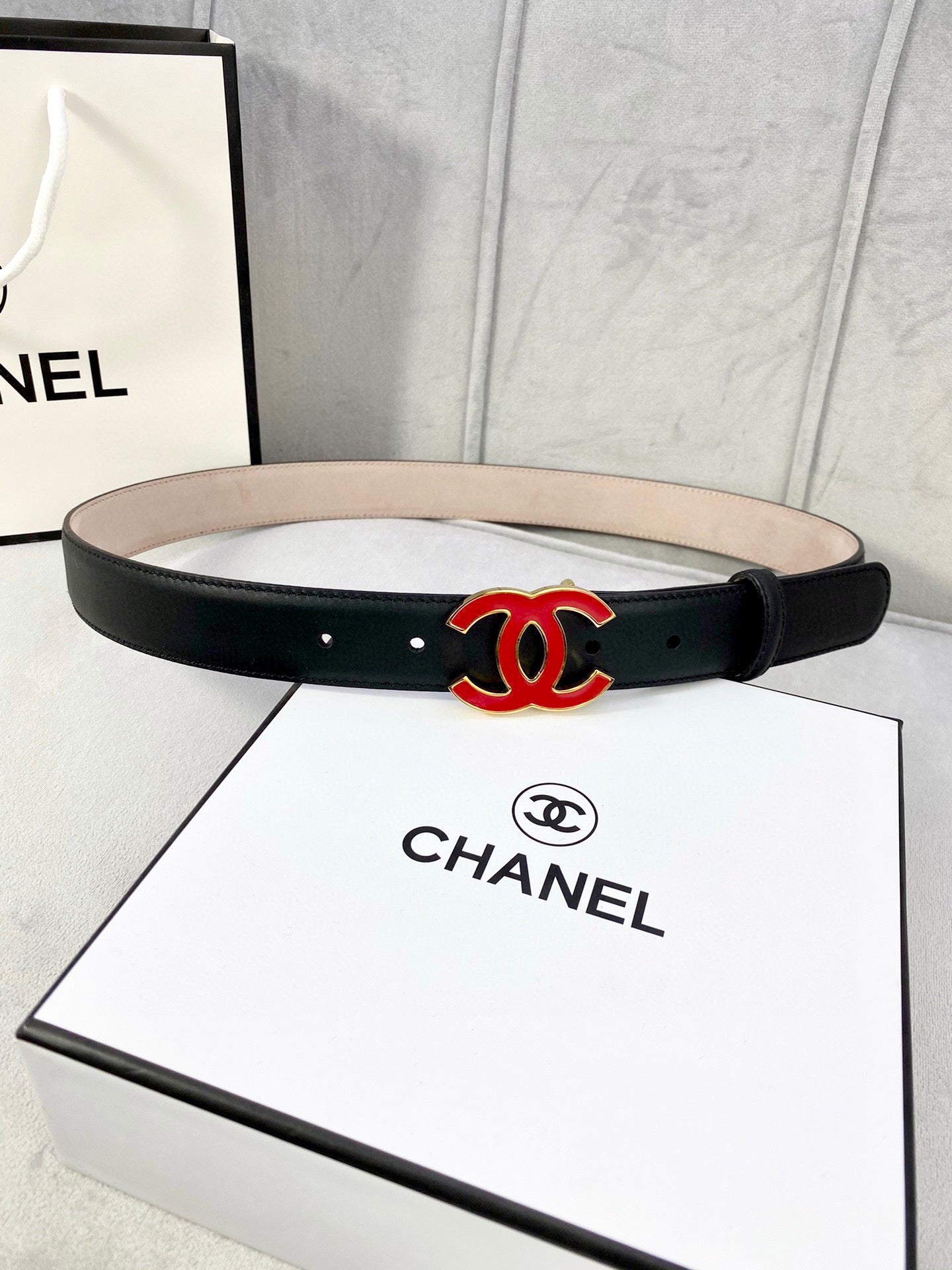 Chanel belt in dark leather with red-and-black CC logo at center, flat strap.