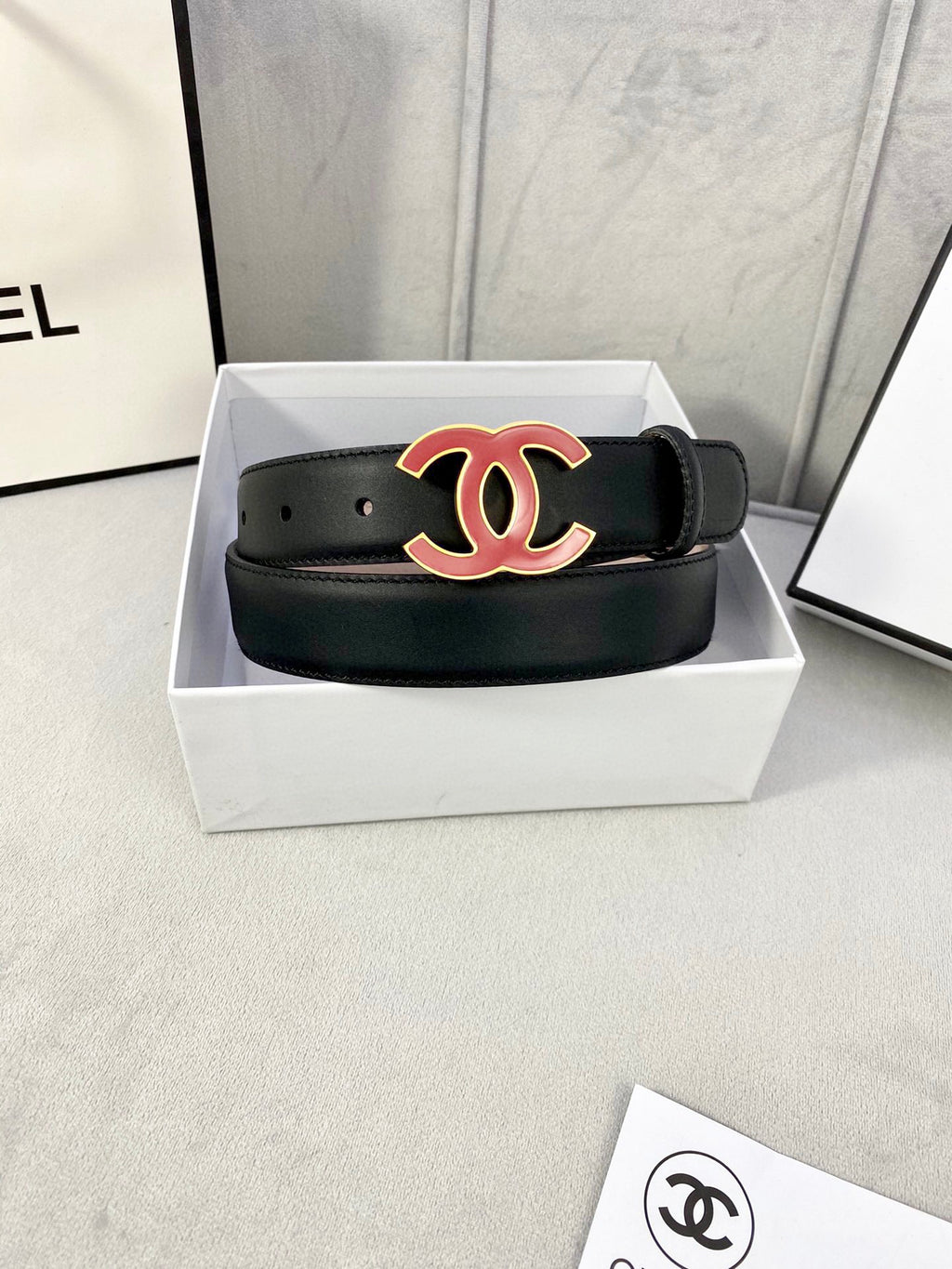 Chanel belt in dark leather with red-and-black CC emblem, laid flat in box.