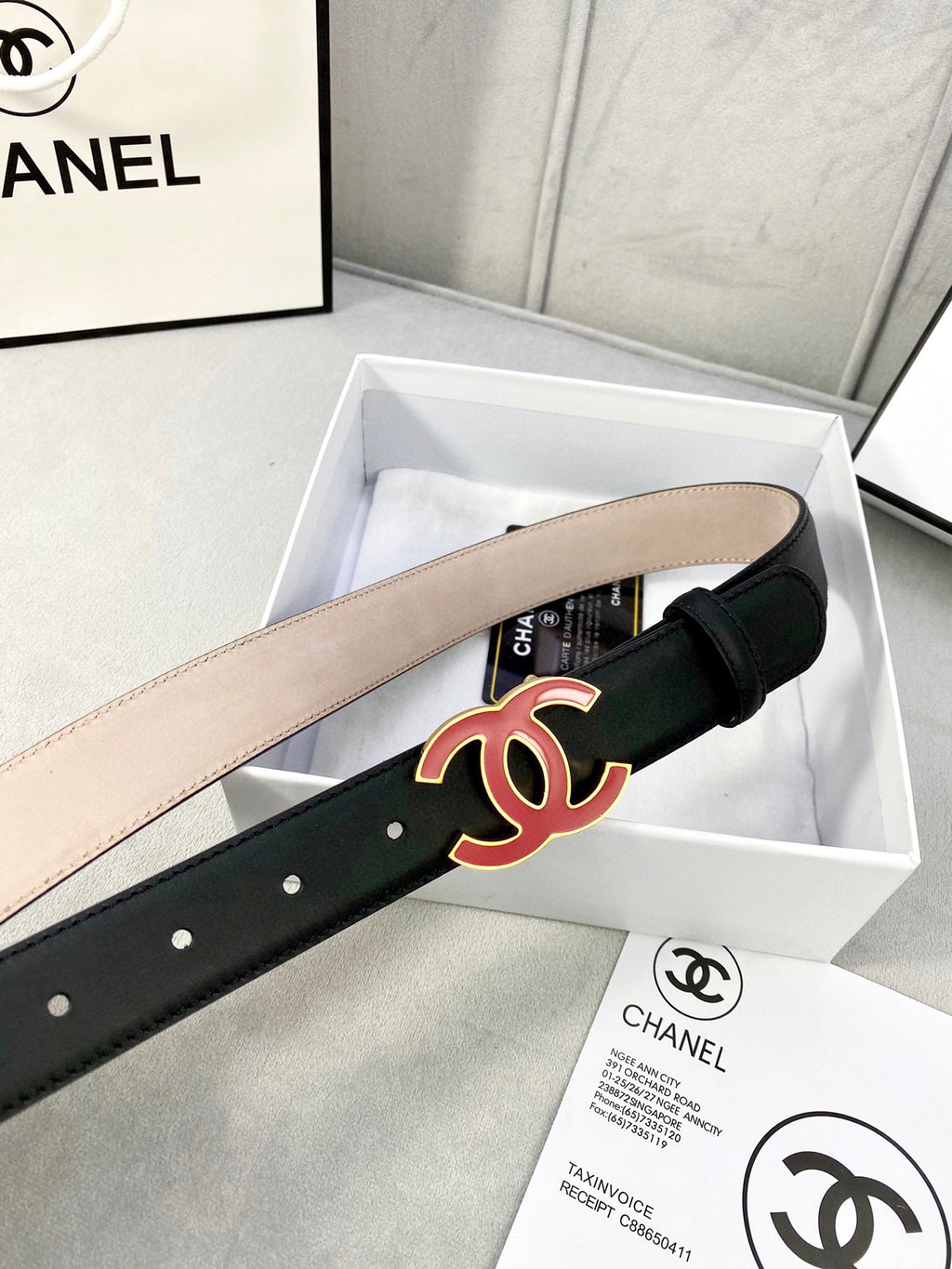Chanel belt in dark leather with red-and-black CC buckle, side view with holes.