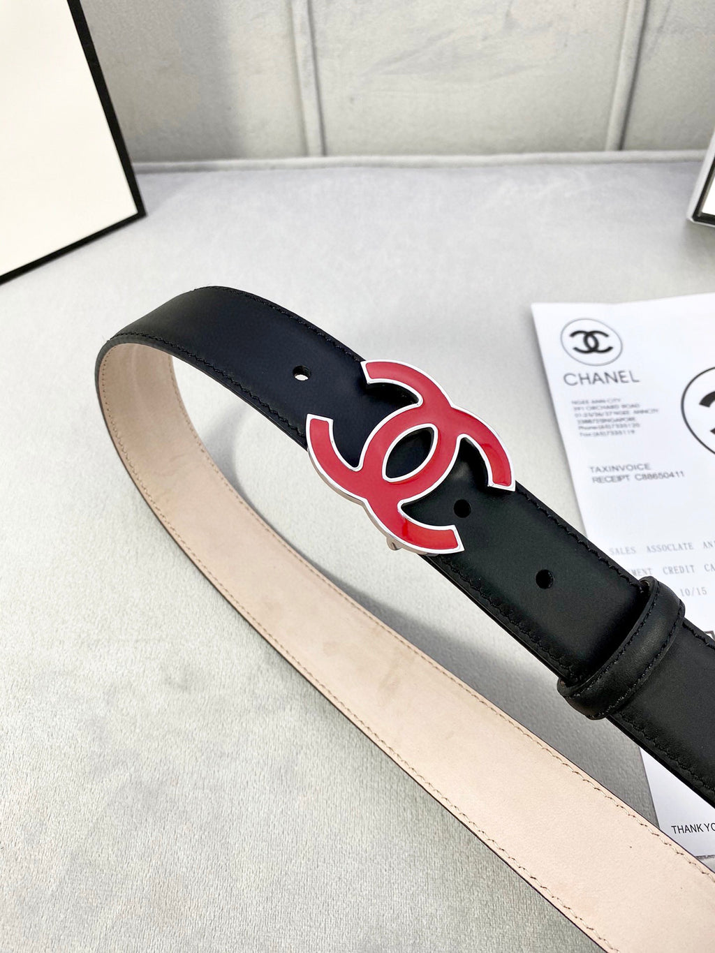 Chanel belt on display: dark leather strap with red-and-black CC emblem and holes.
