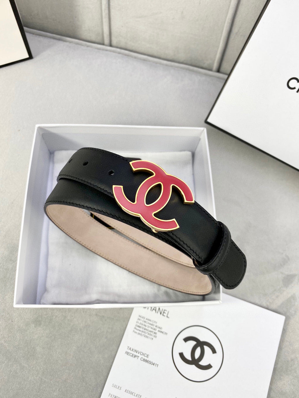 Chanel belt in dark leather with red-and-black CC logo on front, adjustable end.