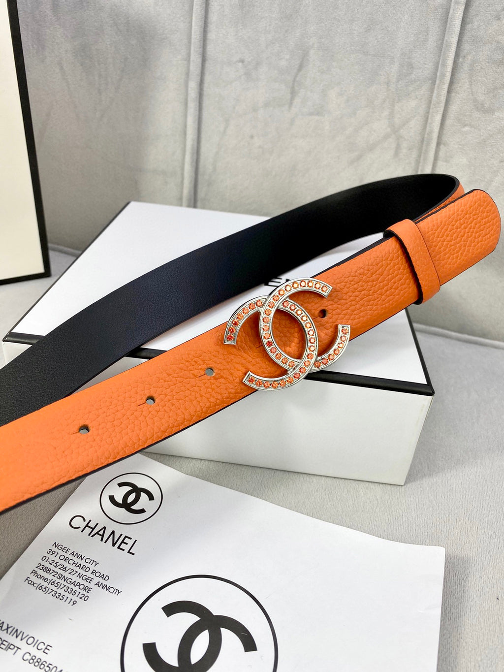 Orange leather belt with gold jeweled buckle and black underside, adjustable strap