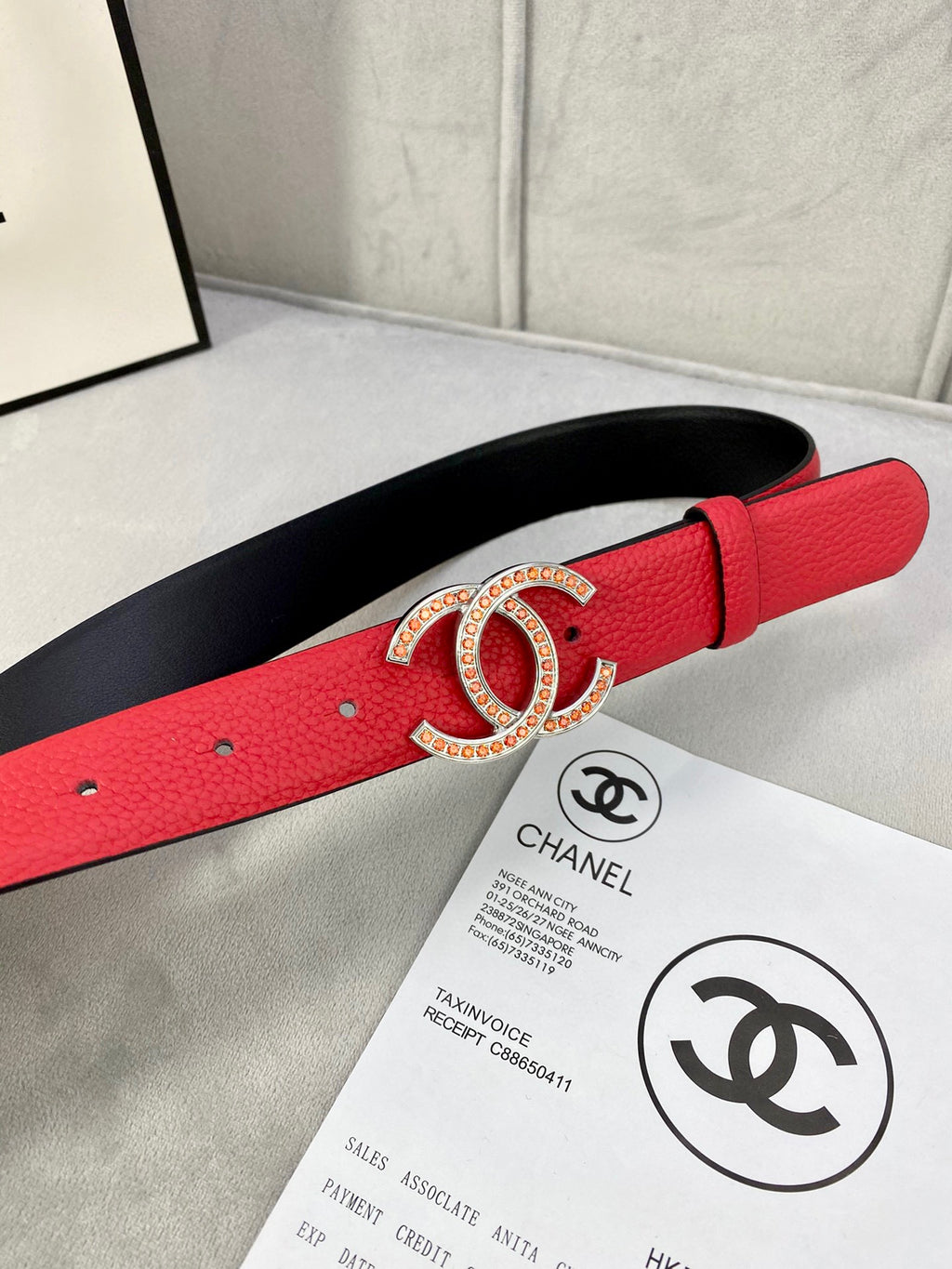 Red leather belt with gold-tone Chanel CC buckle and black underside, close-up.