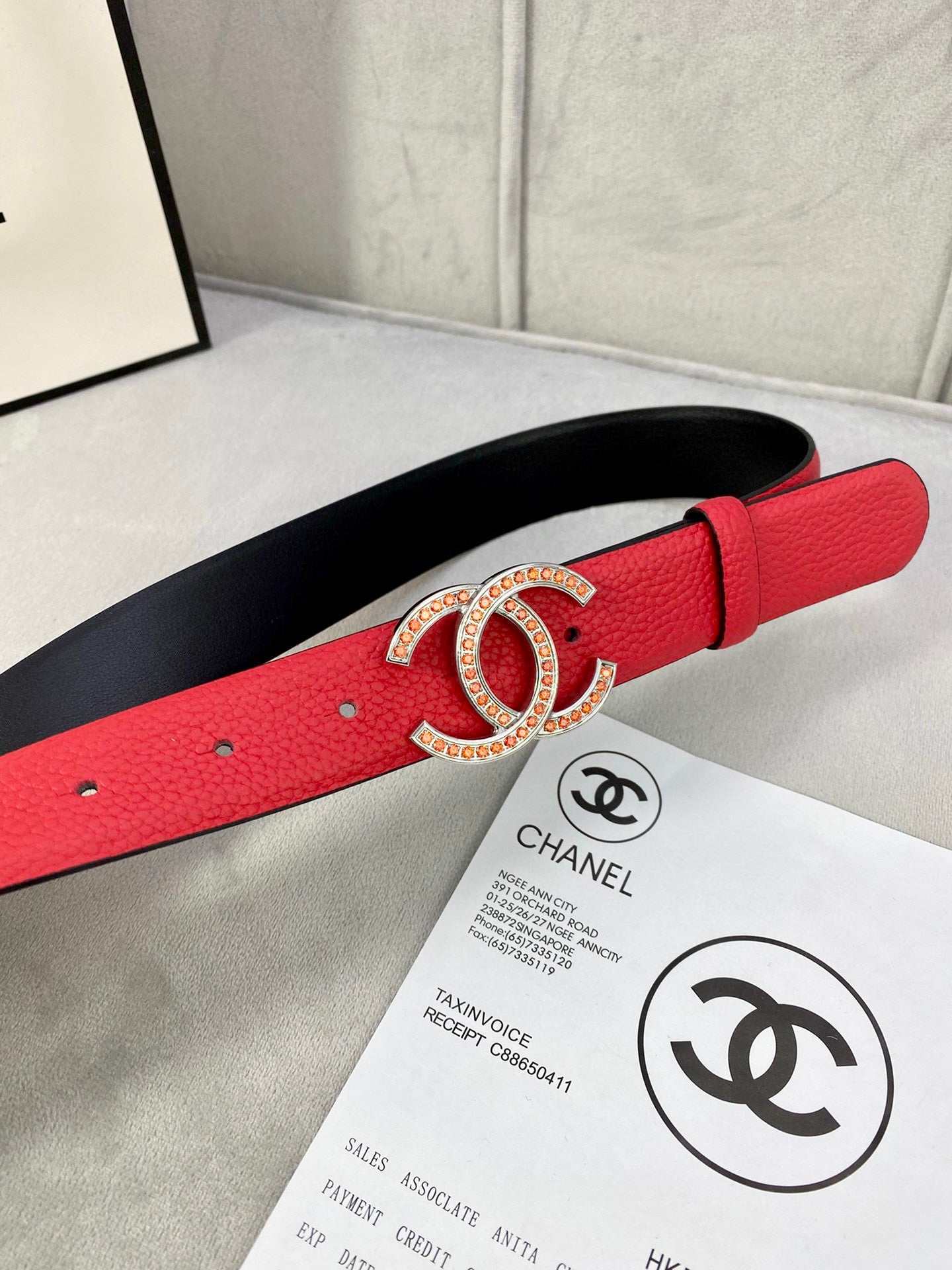 Red leather belt with gold-tone Chanel CC buckle and black underside, close-up.