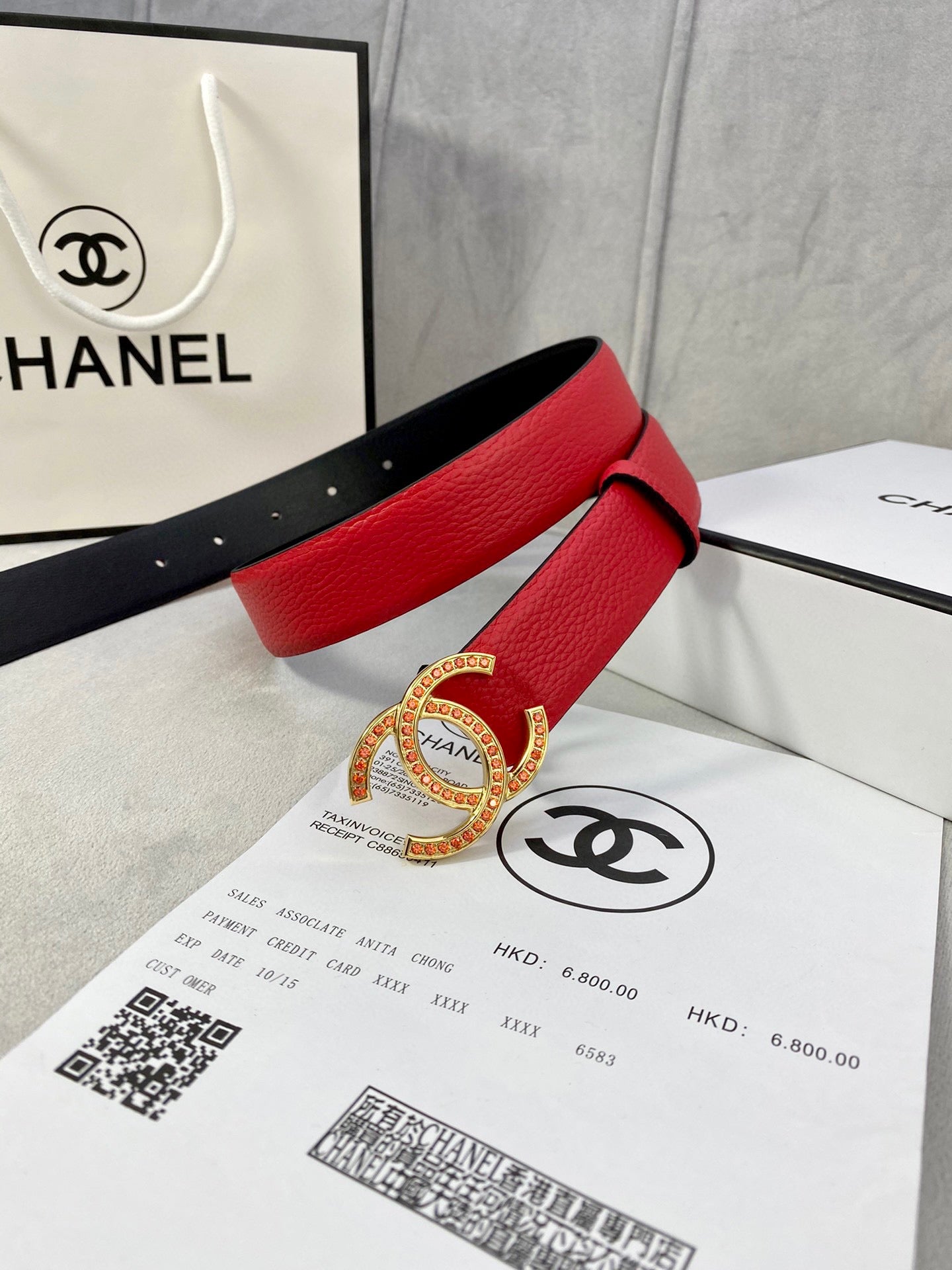 Red leather belt with large Chanel CC buckle, stacked in gift packaging with black strap.