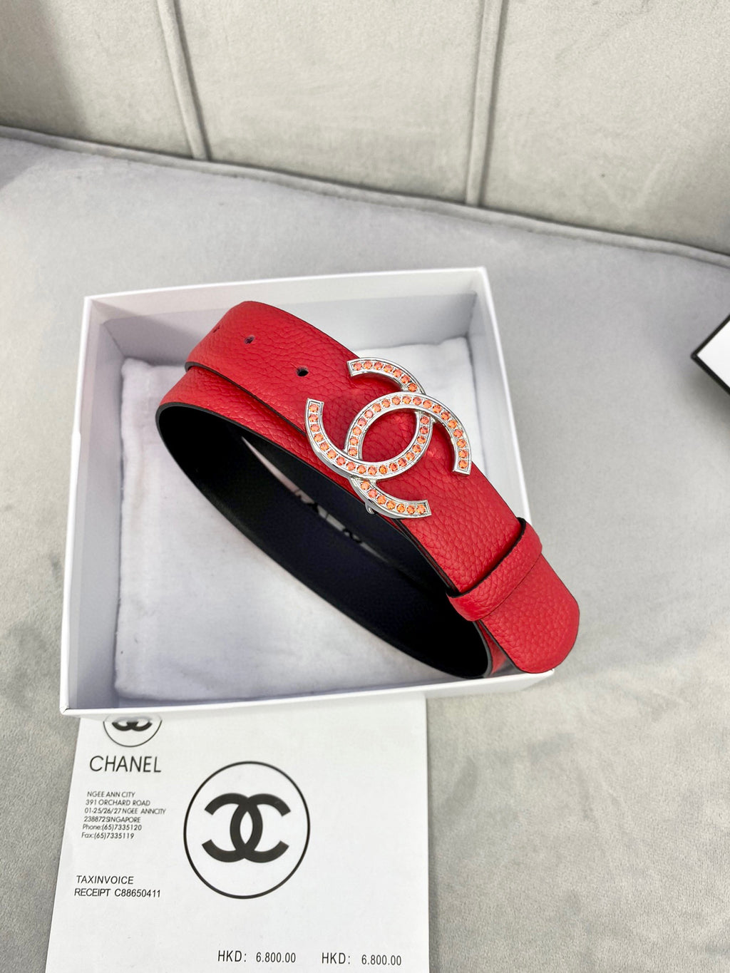 Red leather belt with Chanel CC buckle, set in box with black lining visible.