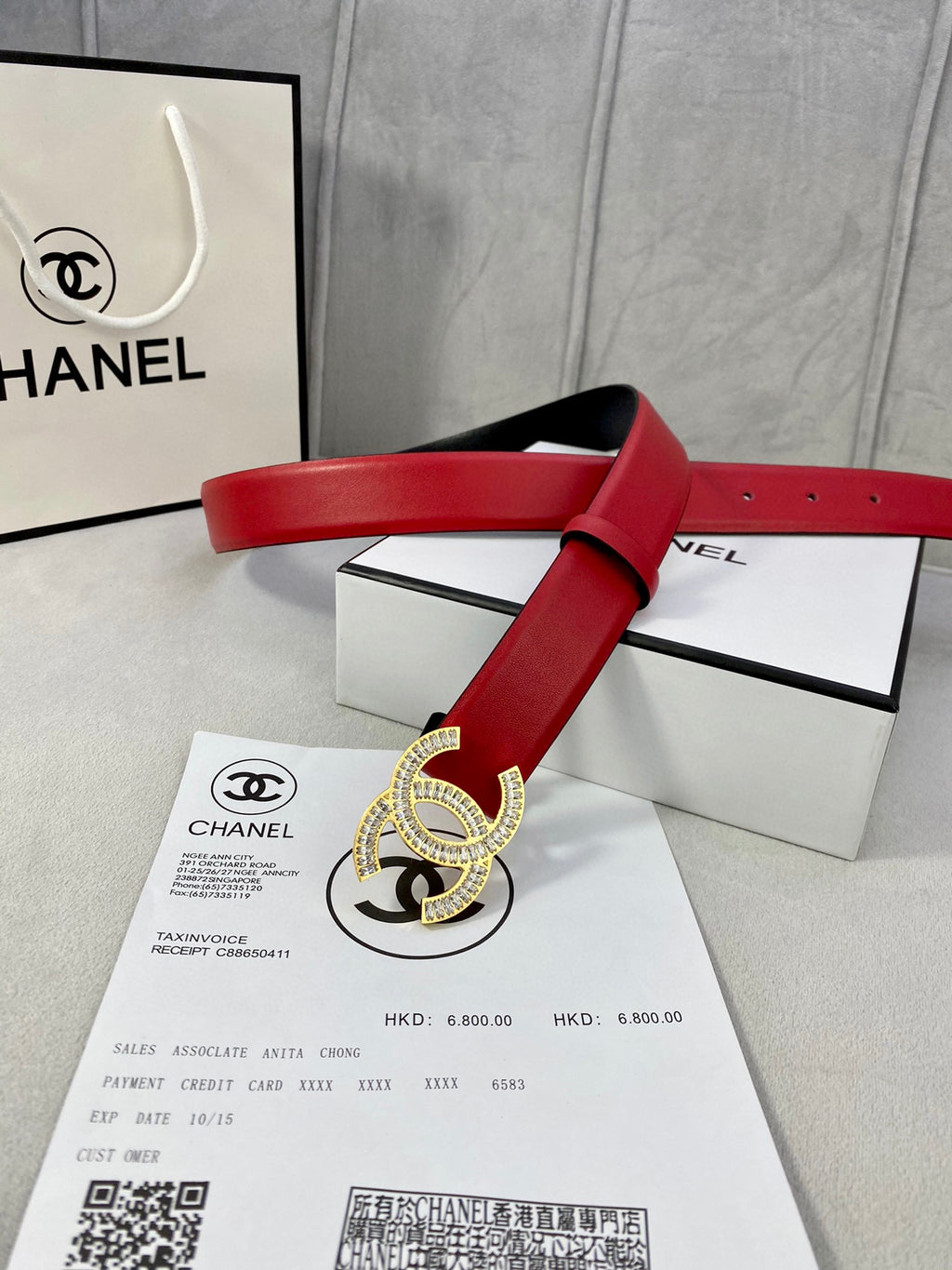 Red leather belt with Chanel gold-tone buckle, laid across product packaging