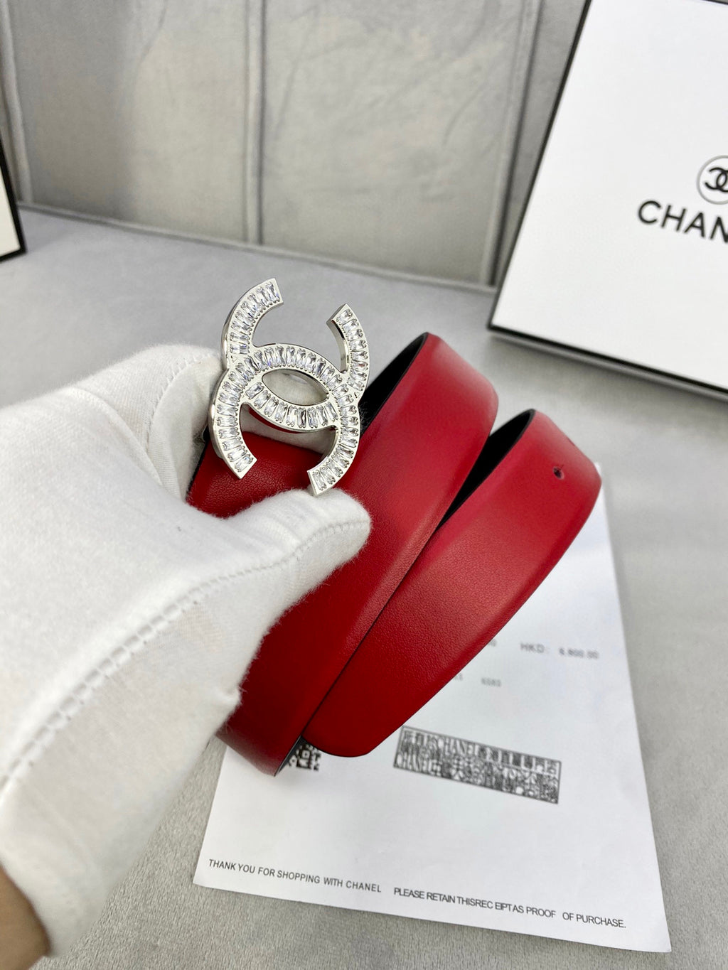 Red leather belt on a white box, featuring a jeweled Chanel gold-tone buckle