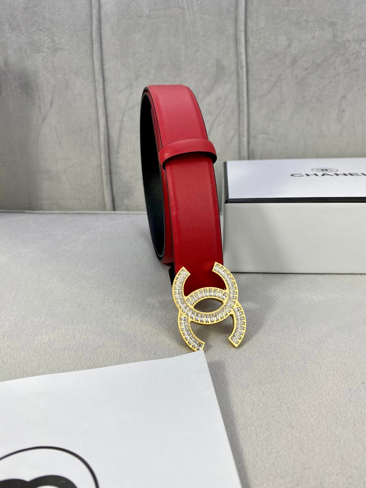 Red leather belt side view with Chanel gold-tone double C buckle on box