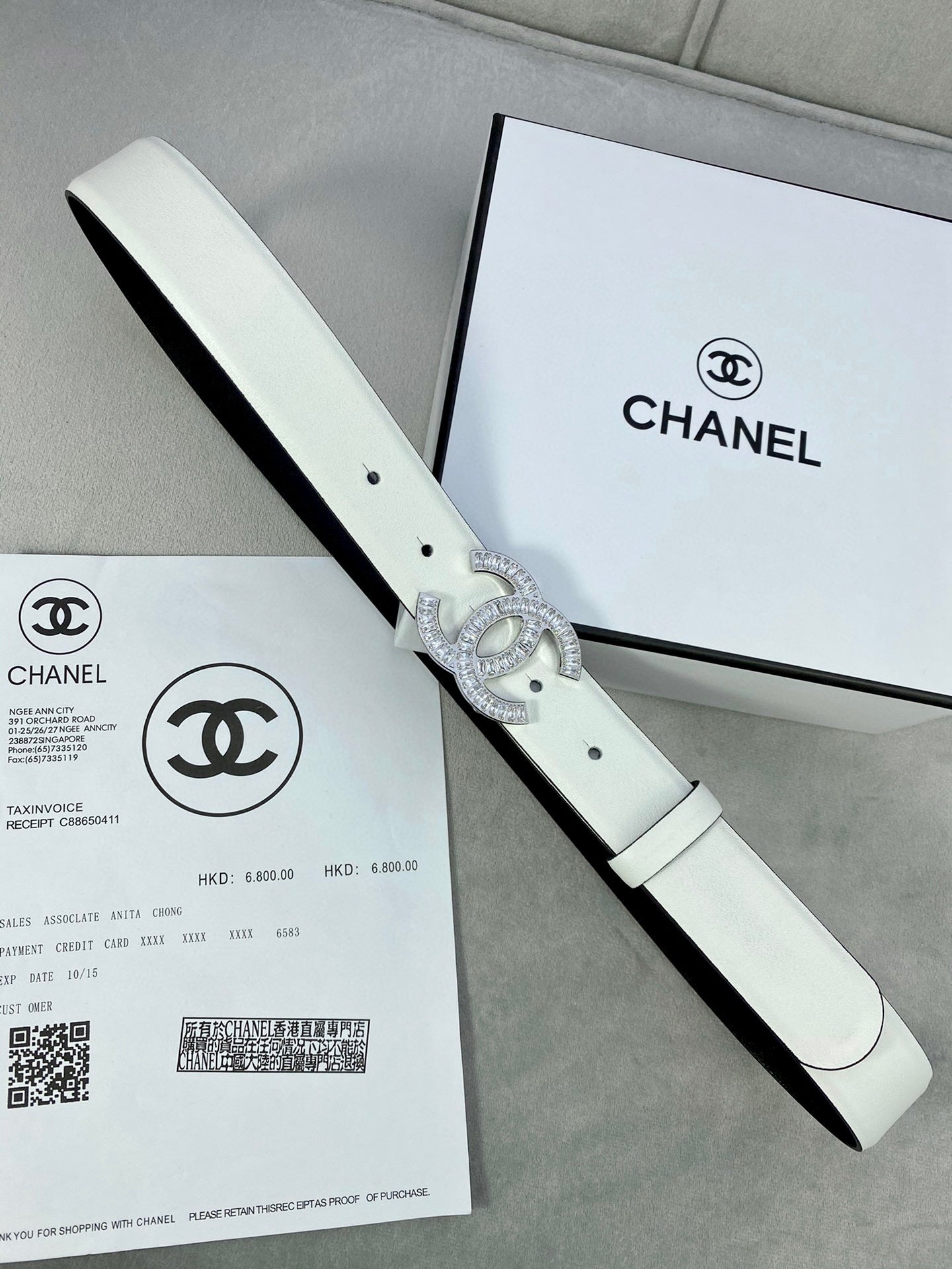 White leather belt with rhinestone CC buckle, shown with a side edge view