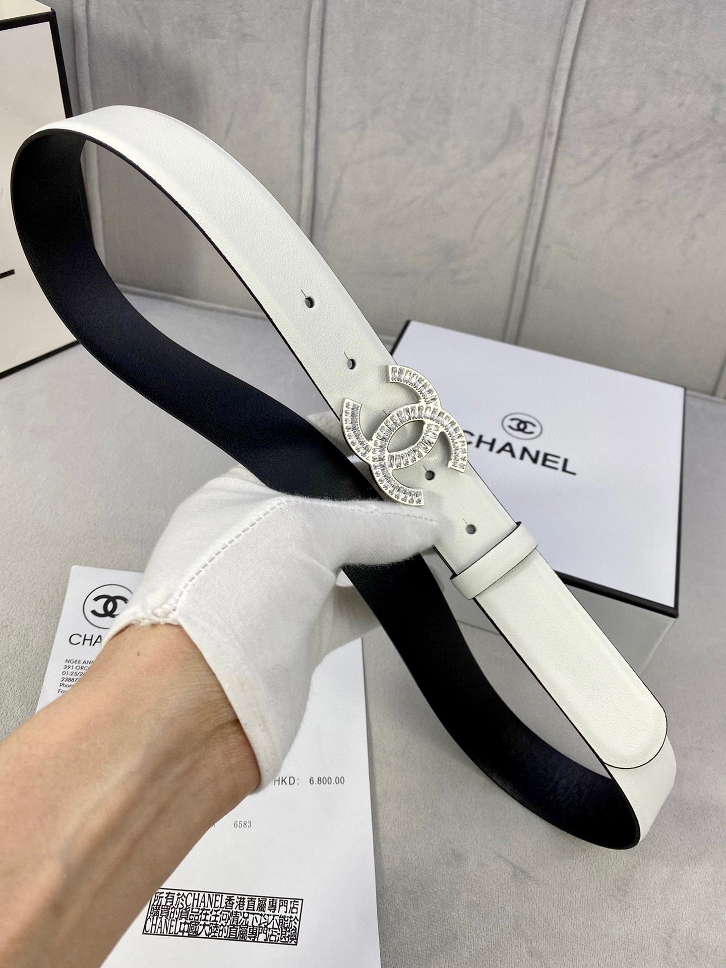 White leather belt with rhinestone CC buckle held in hand over a box