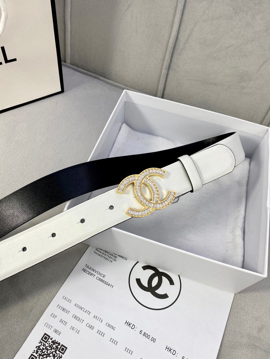 White leather belt with gold-tone CC logo buckle laid in a gift box