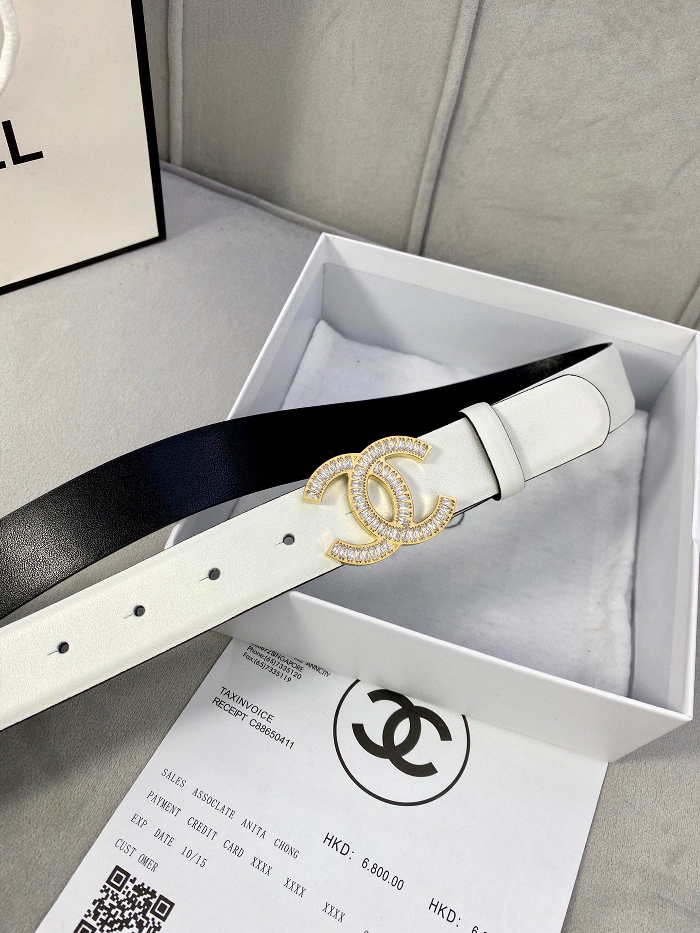 White leather belt with gold-tone CC logo buckle laid in a gift box