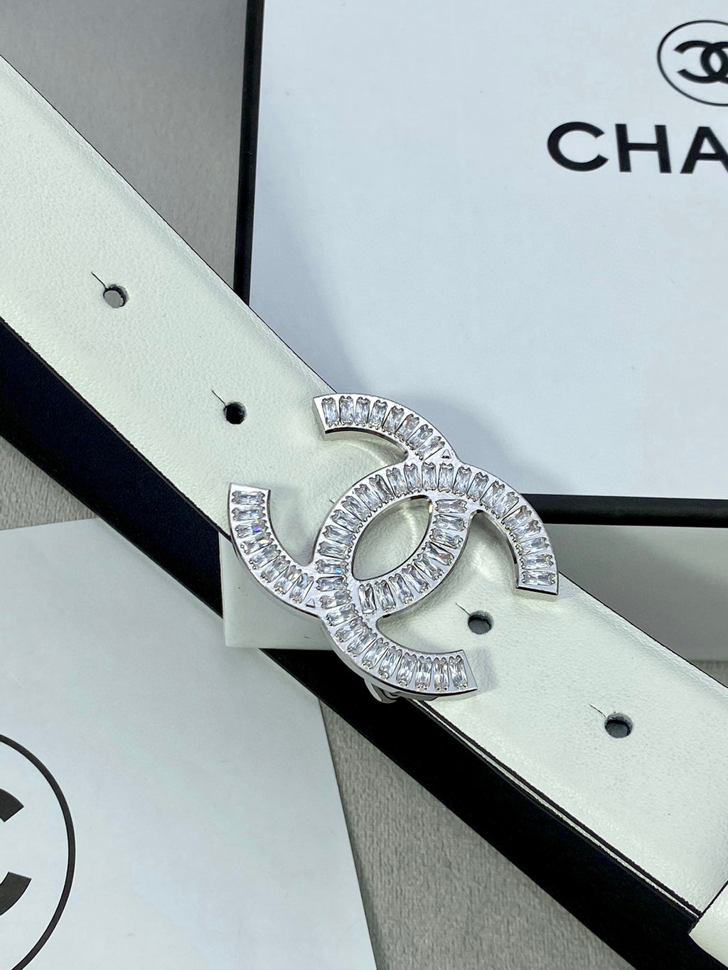 Close-up of white leather belt with rhinestone CC logo buckle and buckle detail