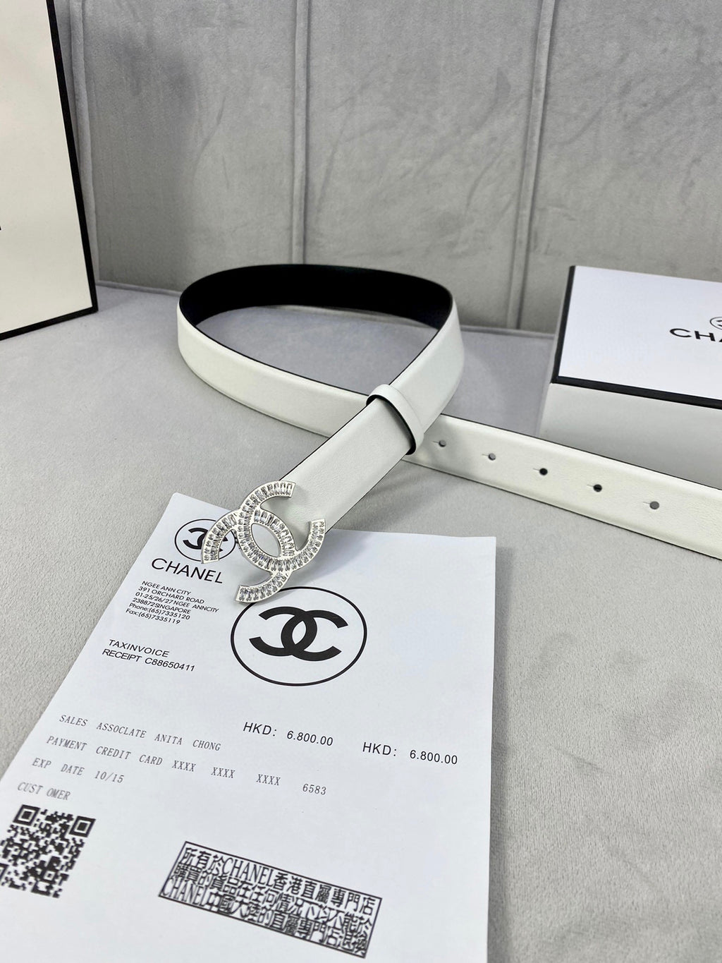 White leather belt with rhinestone CC logo buckle laid flat beside packaging