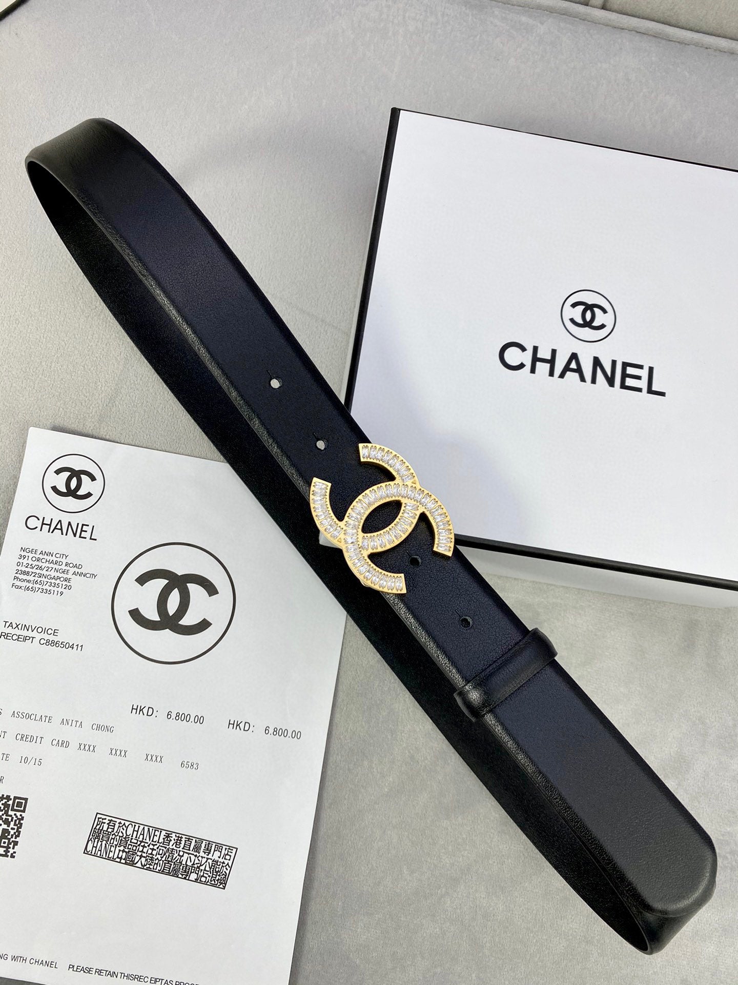Black leather belt with rhinestone CC buckle and long strap, with a retail box nearby