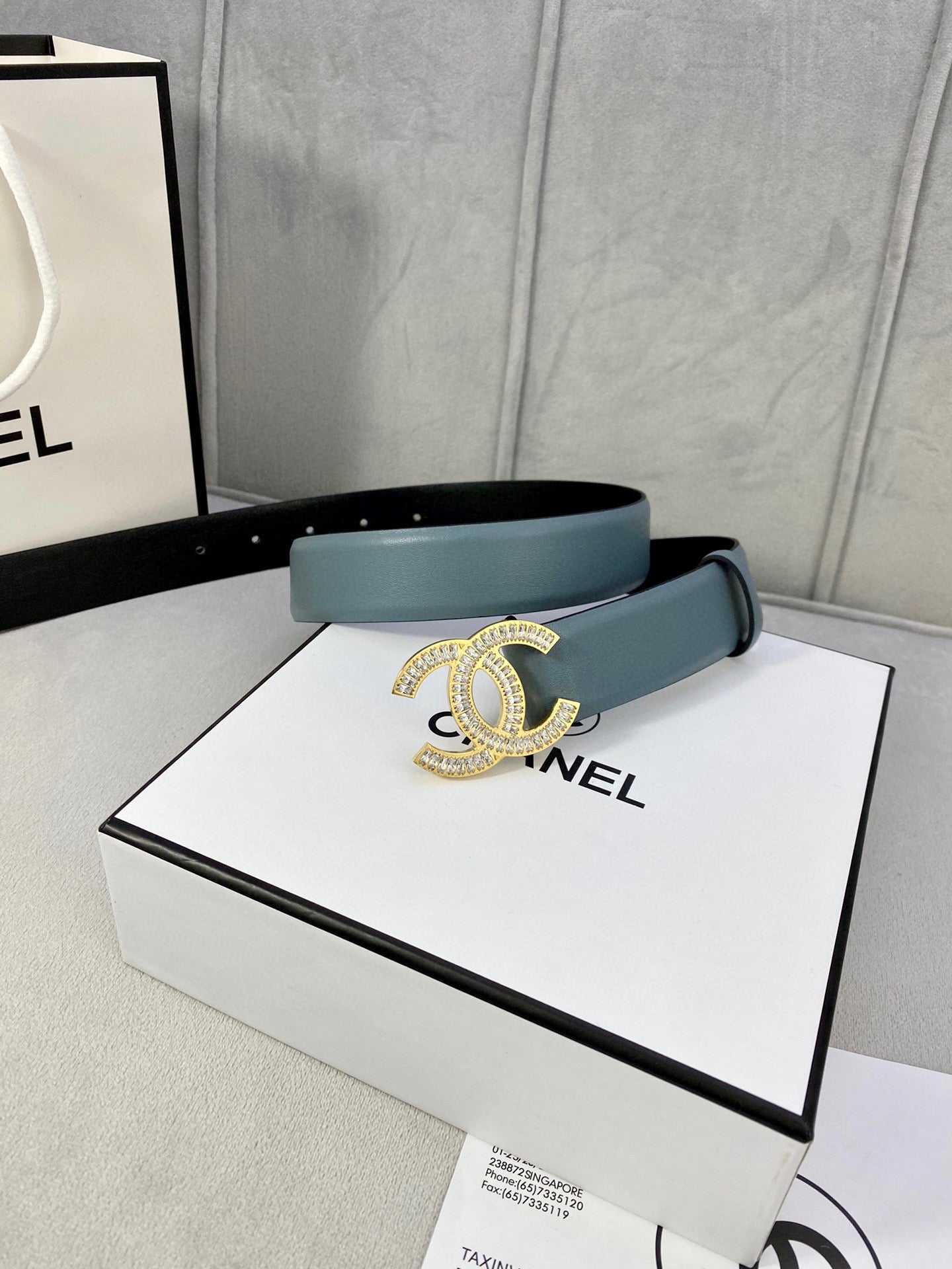 Light blue Chanel belt with gold-toned CC buckle on top of a shopping box.